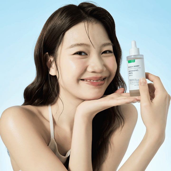 Nasmejana ženska drži Eqqualberry Swimming Pool Ampoule, vlažilni izdelek za nego kože, z obema rokama na svetlo modri podlagi.