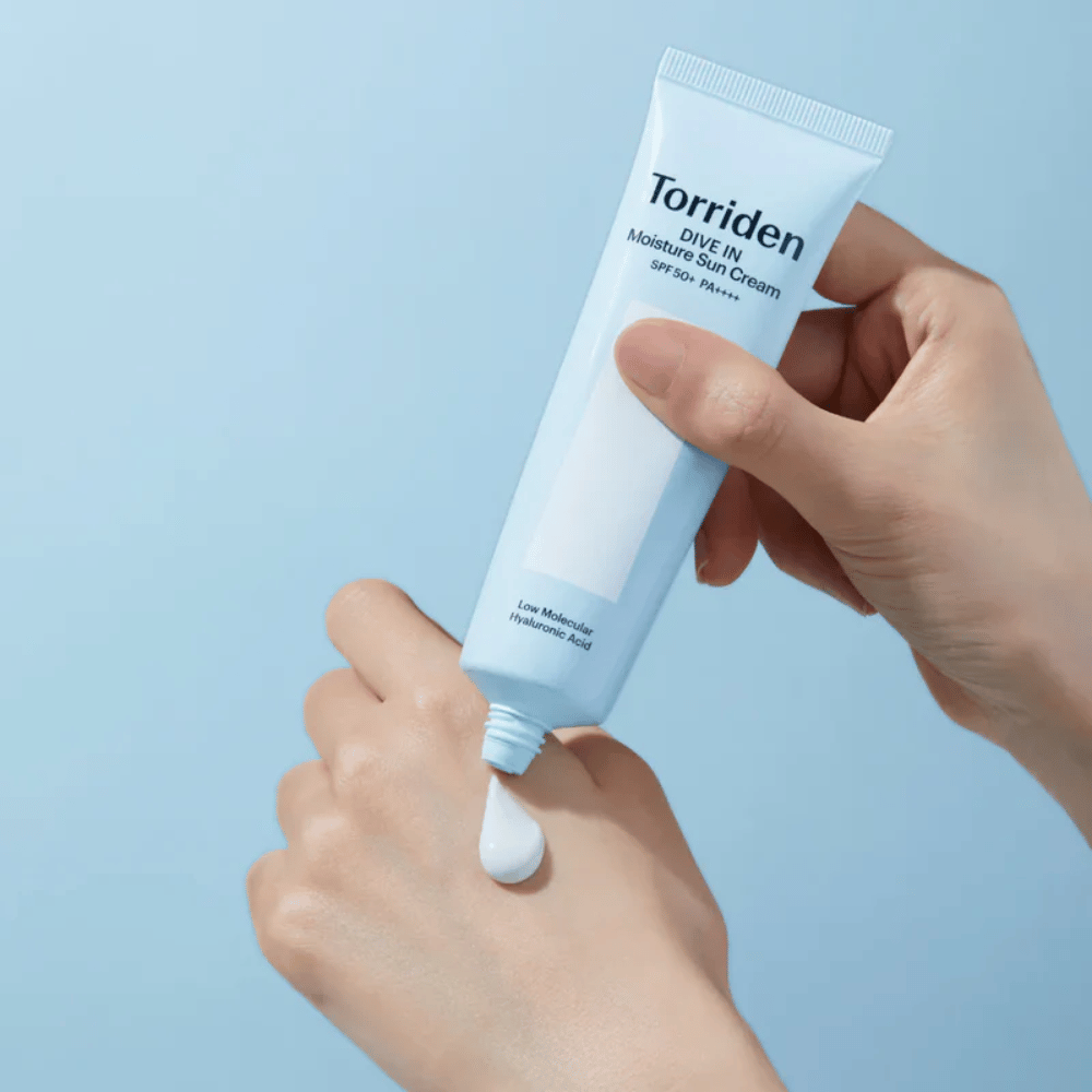 Torriden DIVE-IN Moisture Sun Cream SPF50+ PA++++ se nanese na roko, da prikaže lahko in kremasto teksturo vlažilne kreme za sončenje.