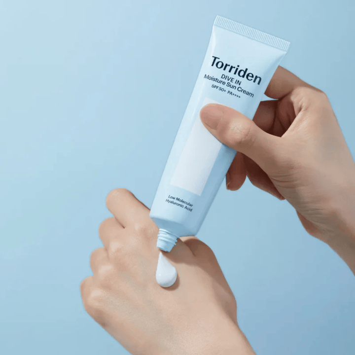 Torriden DIVE-IN Moisture Sun Cream SPF50+ PA++++ se nanese na roko, da prikaže lahko in kremasto teksturo vlažilne kreme za sončenje.