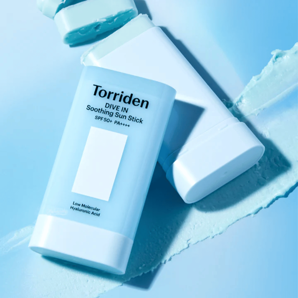 Torriden DIVE IN Soothing Sun Stick SPF50+ PA++++ skupaj z razmazano teksturo izdelka, ki ponazarja vlažilni učinek in lahkoten nanos.