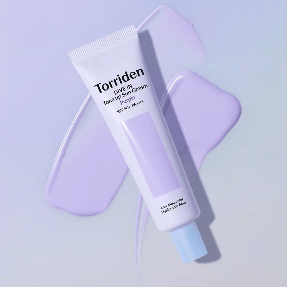 Torriden DIVE IN Tone Up Sun Cream Purple postavljena na razmazano vijolično kremo, ki poudarja učinek izenačevanja tena in sijaja.