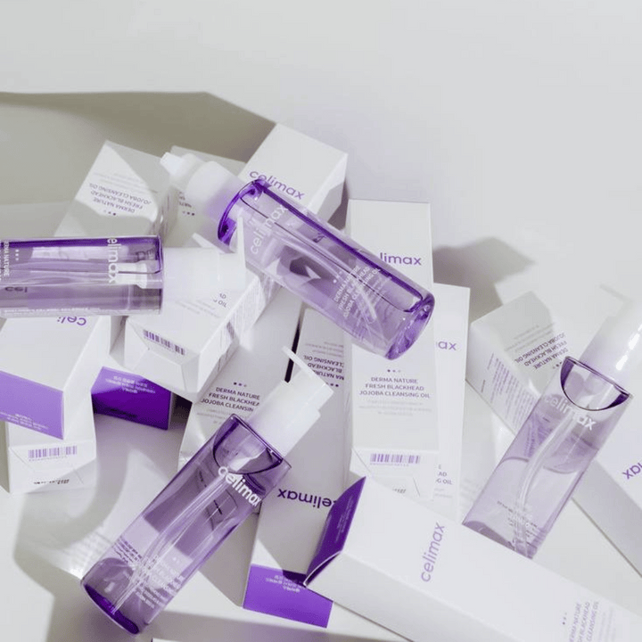 Celimax Derma Nature Fresh Blackhead Jojoba Cleansing Oil v vijoličnih steklenicah, postavljenih med bele embalaže izdelkov z vijoličnimi detajli.