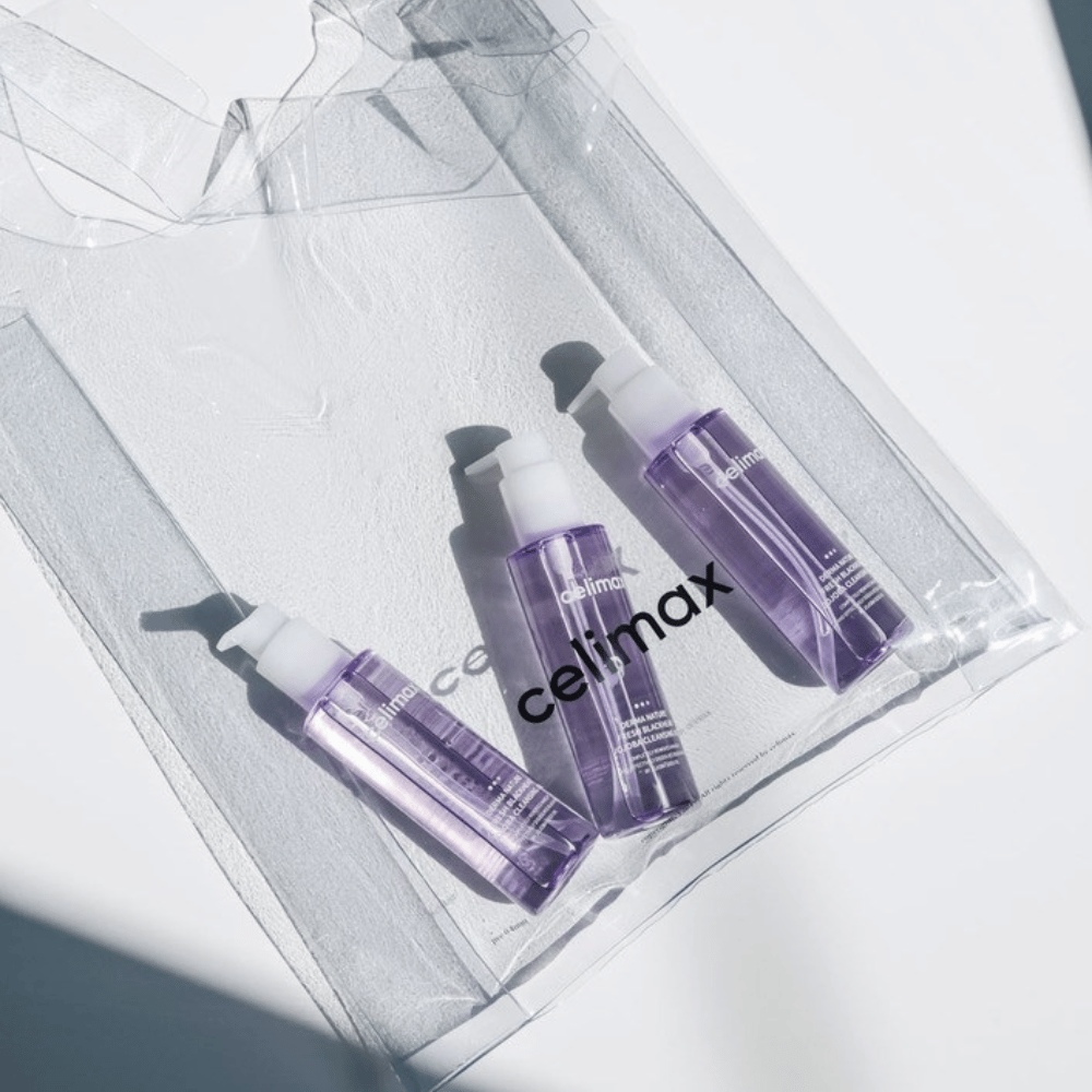 Tri steklenice Celimax Derma Nature Fresh Blackhead Jojoba Cleansing Oil v vijolični embalaži, postavljene v prozorno vrečko z logotipom 'celimax'.