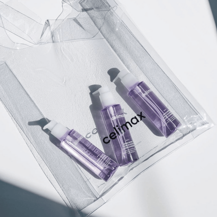 Tri steklenice Celimax Derma Nature Fresh Blackhead Jojoba Cleansing Oil v vijolični embalaži, postavljene v prozorno vrečko z logotipom 'celimax'.