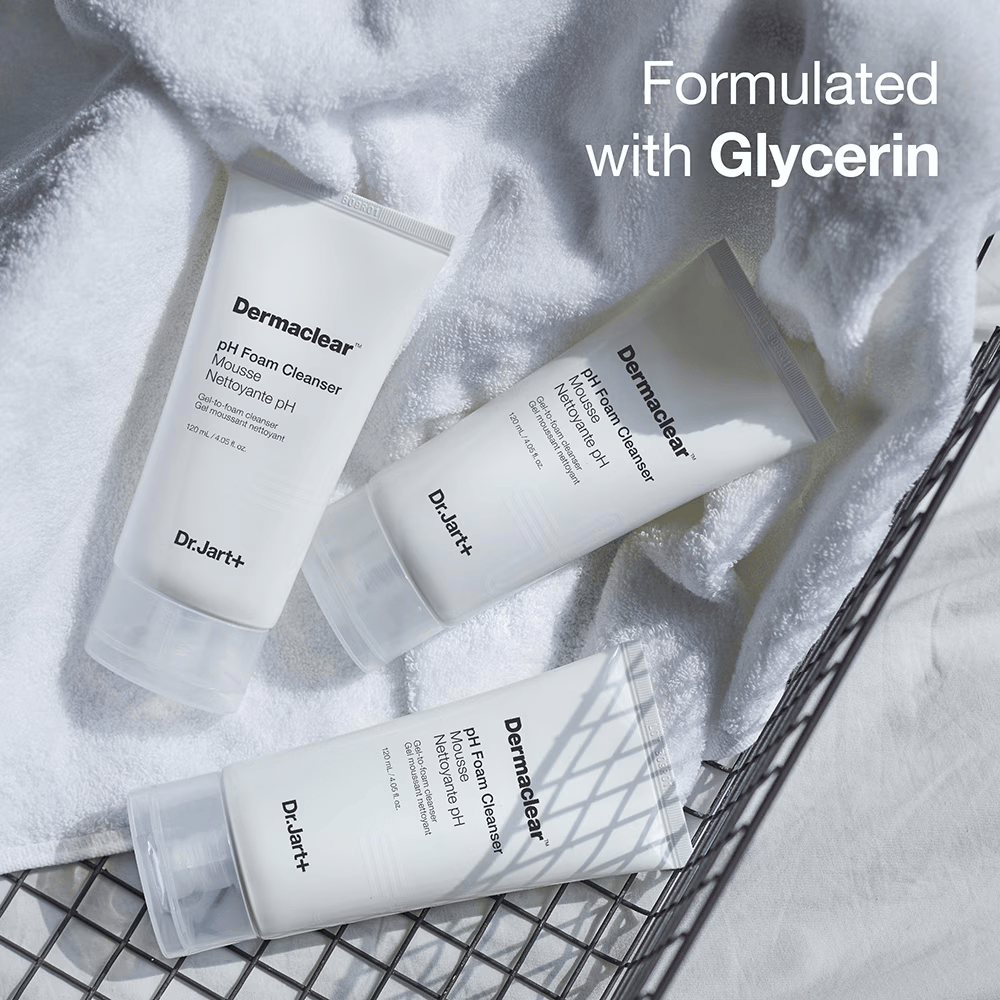 Tri tube Dr.Jart+ Dermaclear pH Foam Cleanser ležijo na beli frotirni brisači v kovinski košari, z besedilom "Formulated with Glycerin" v zgornjem kotu.