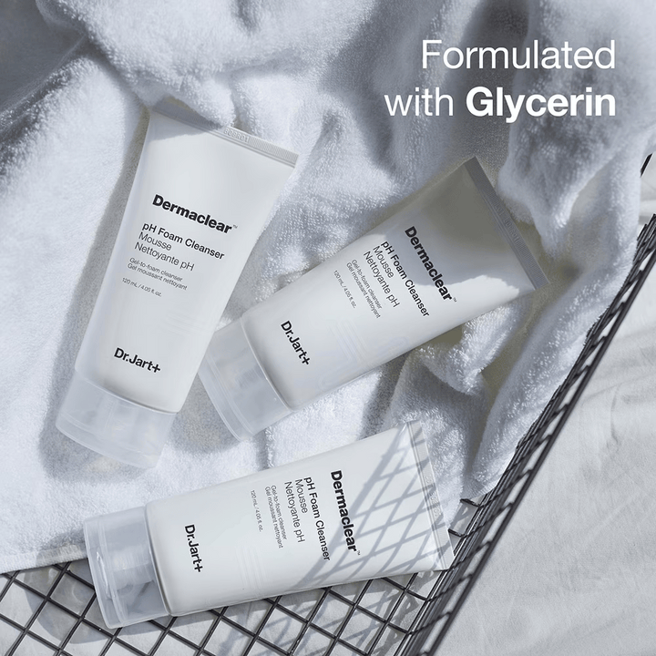 Tri tube Dr.Jart+ Dermaclear pH Foam Cleanser ležijo na beli frotirni brisači v kovinski košari, z besedilom "Formulated with Glycerin" v zgornjem kotu.