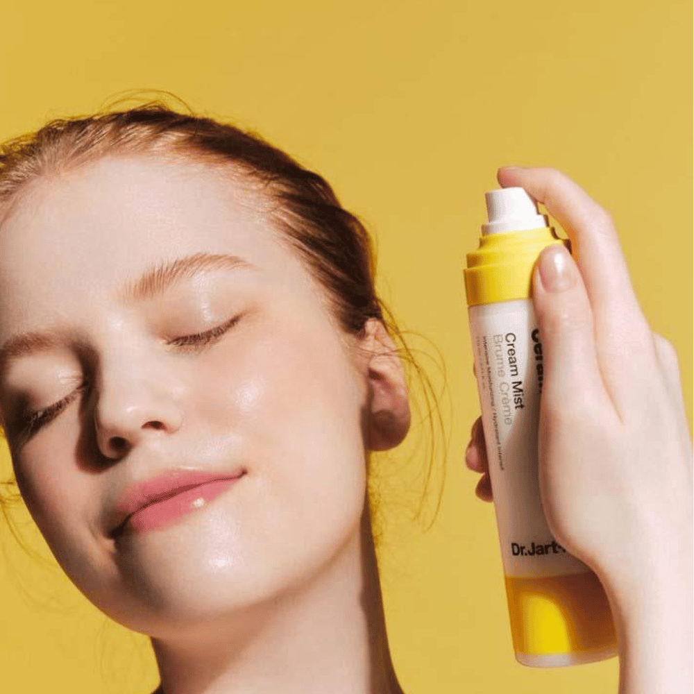 Ženska drži steklenico Dr. Jart+ Ceramidin Cream Mist 110ml ob obrazu, kar poudarja njene vlažilne prednosti in vegansko formulacijo.