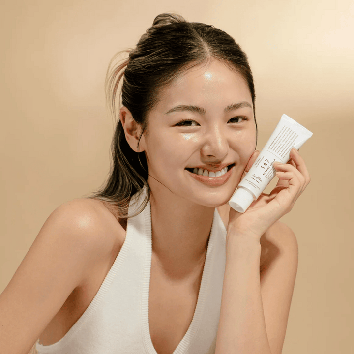 Model z sijočo kožo, ki se smeji in drži Dr. Althea 147 Barrier Cream – korejska krema za obraz za kožno bariero in vlaženje.