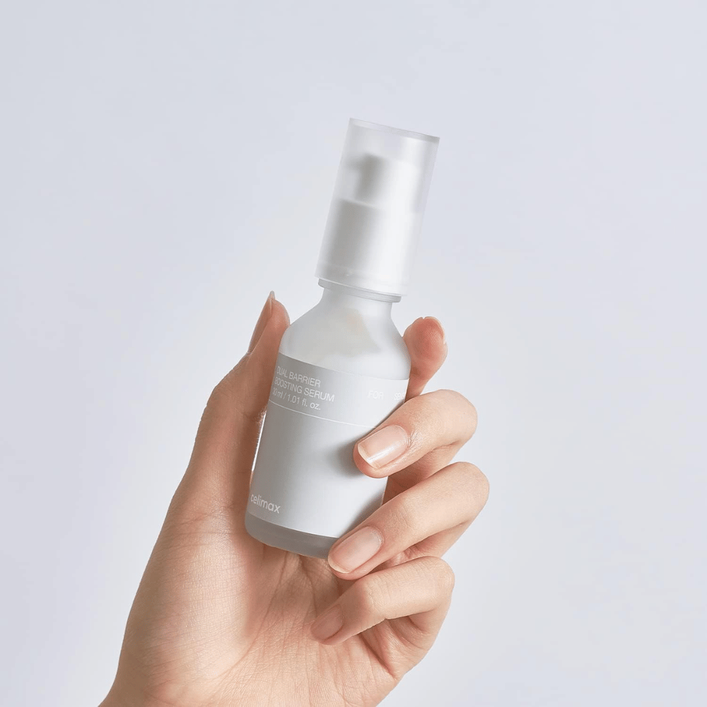 Celimax Dual Barrier Boosting Serum v roki, minimalistična embalaža, ki prikazuje korejski serum za krepitev pregrade za občutljivo kožo.