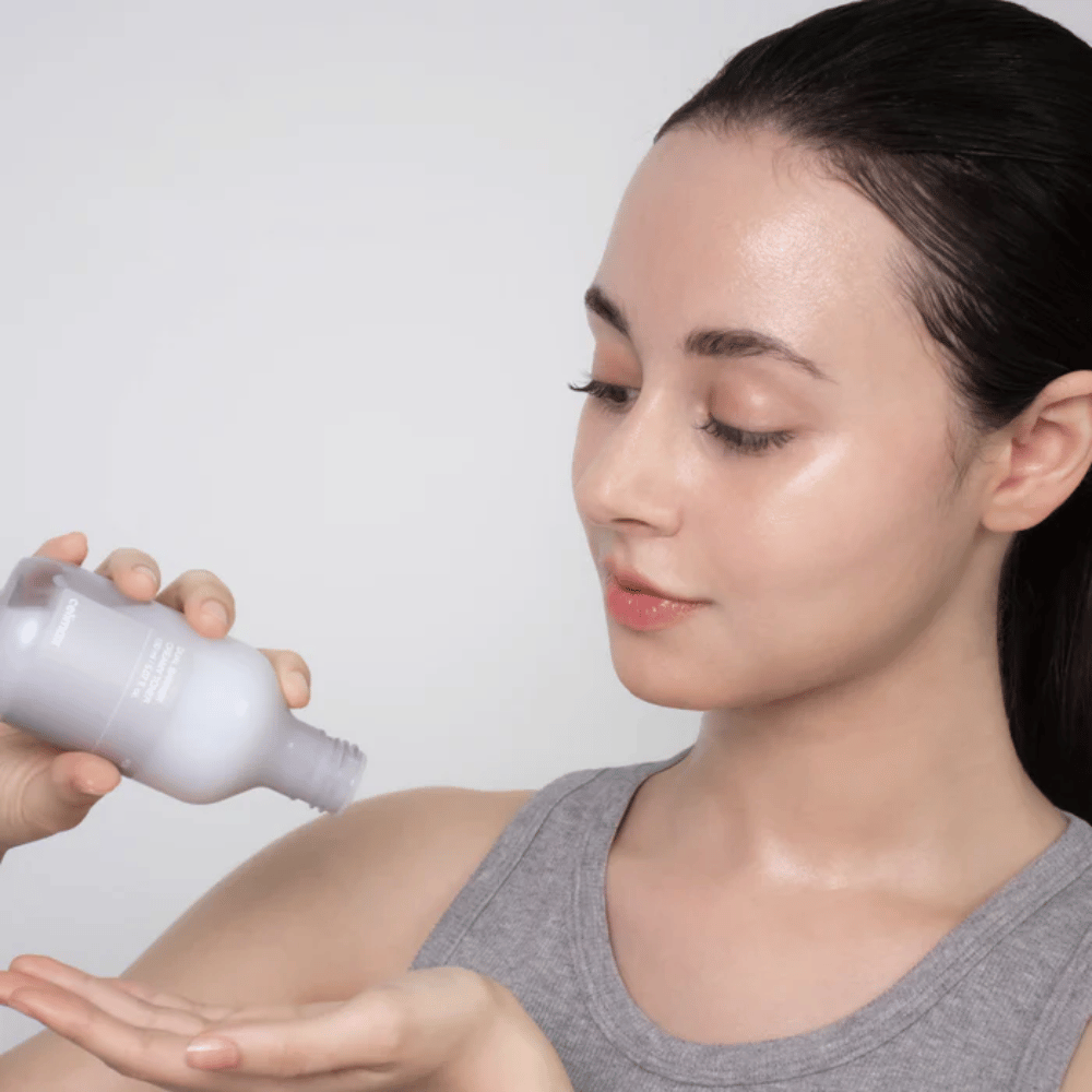 Ženska z sijočo, navlaženo kožo nanese Celimax Dual Barrier Creamy Toner tako, da izdelek vlije v dlan pred svojo rutino nege kože.