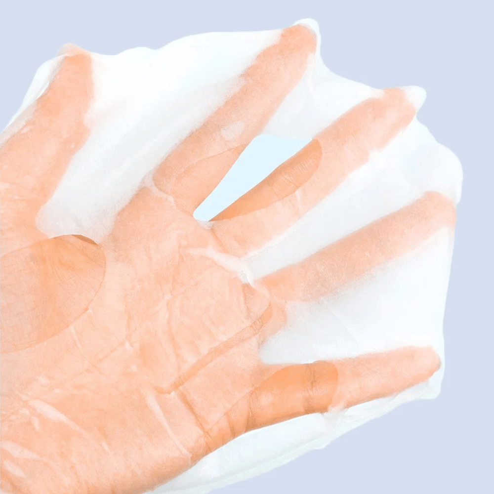 Prozorna in vlažna obrazna maska je držana na roki proti svetlo modrem ozadju. Maska je zasnovana tako, da pokrije obraz z odprtinami za oči in usta.