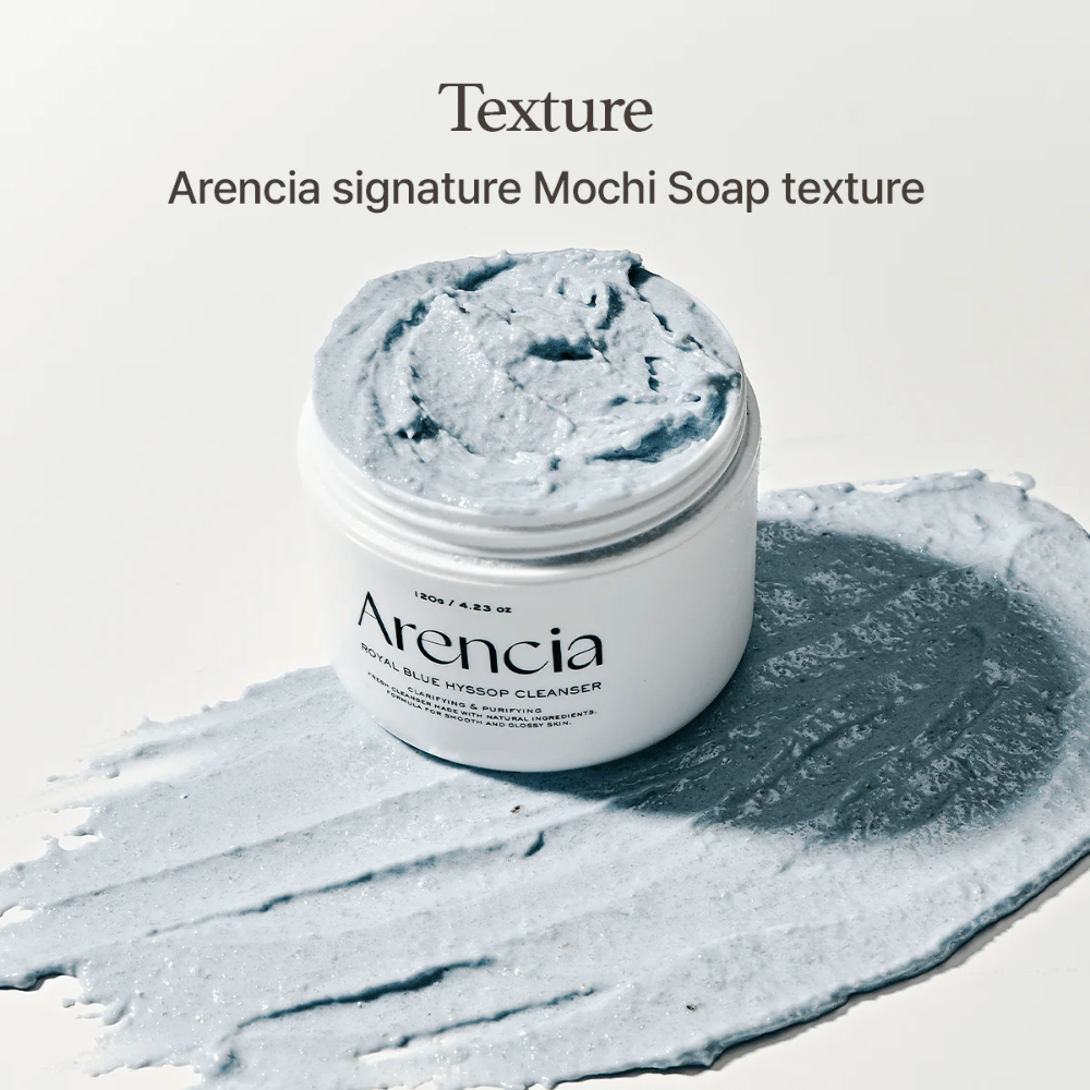 Odprt kozarec z Arencia Fresh Blue Hyssop Rice Mochi Cleanser, postavljen na razmazan sloj modre, kremaste čistilne formule, ki prikazuje njeno mochi podobno teksturo.