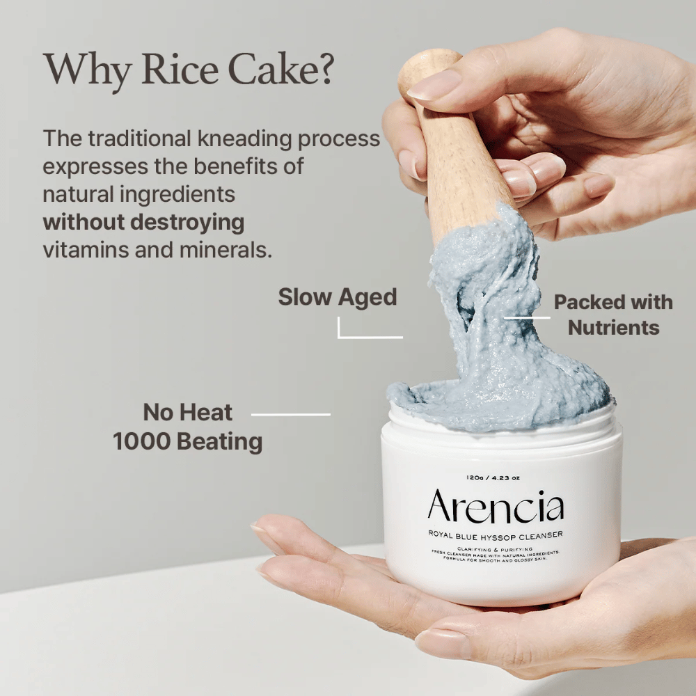 Roka, ki drži čistilni kozarec "Arencia Royal Blue Hyssop Cleanser" z leseno žlico, ki dviguje modro, mochi podobno čistilno pasto. Besedilo na sliki opisuje prednosti postopka z riževo pasto, kot so "No Heat", "1000 Beating", "Slow Aged" in "Packed with Nutrients".
