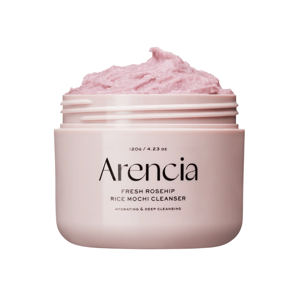 Približan posnetek roza lončka z Arencia Royal Rosehip Cleanser, napolnjenega z roza čistilno kremo z teksturo, podobno stepanemu mochi. Besedilo na lončku kaže, da izdelek vlaži in globinsko čisti.