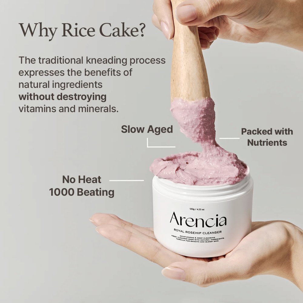 Roka drži odprt lonček Arencia Royal Rosehip Cleanser, z roza, mochi podobno čistilno formulo, ki jo dviguje z leseno lopatico - prikazuje teksturo izdelka in tradicionalno metodo izdelave.