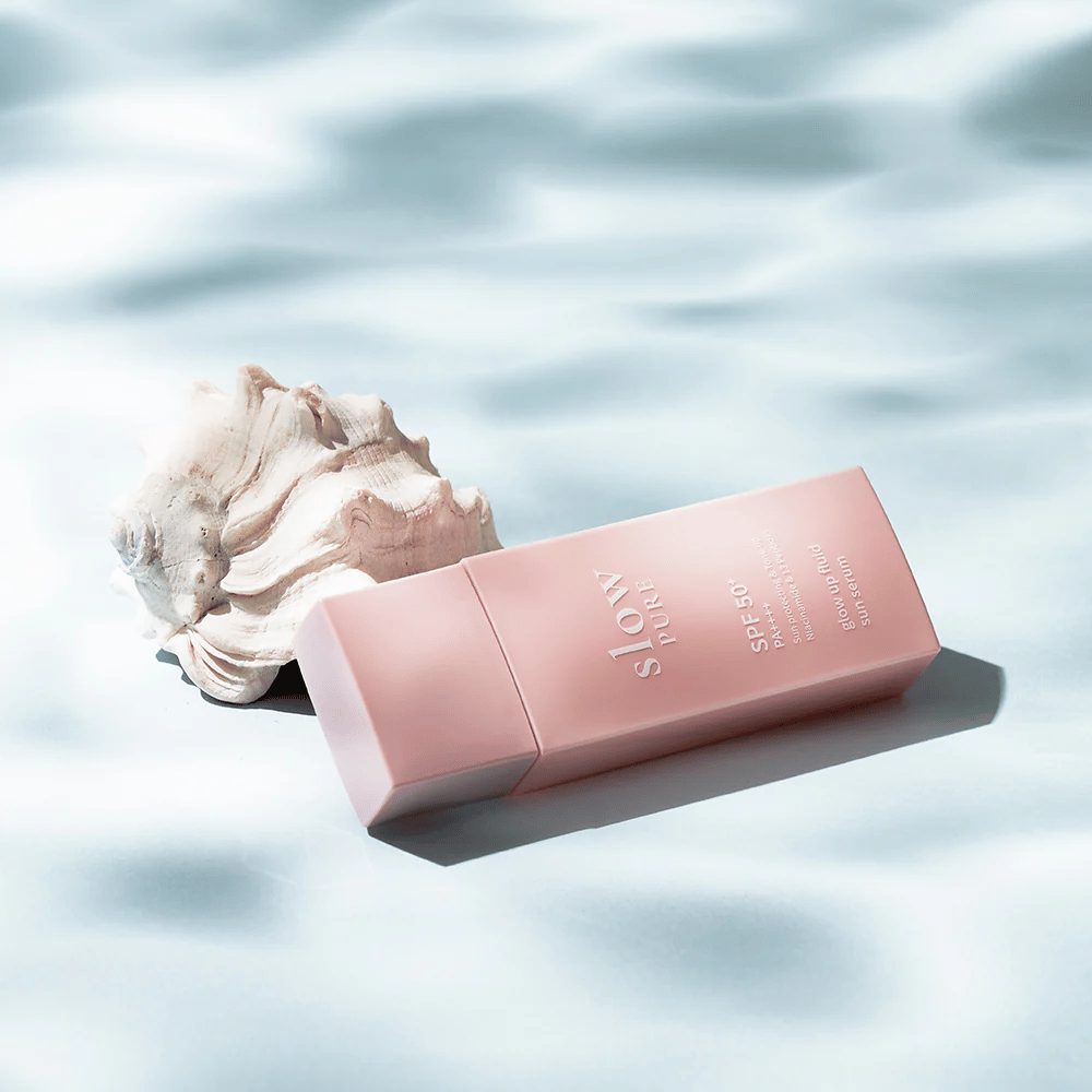 Slow Pure Glow Up Fluid Sun Serum ob školjki in vodnem učinku, poudarja zaščito pred soncem in sijaj.