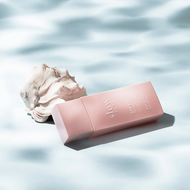 Slow Pure Glow Up Fluid Sun Serum ob školjki in vodnem učinku, poudarja zaščito pred soncem in sijaj.