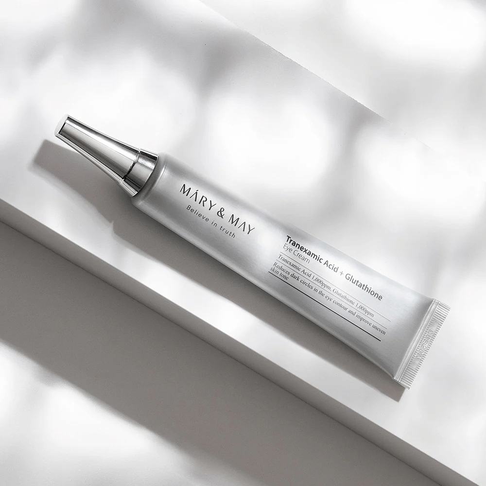 Bližnji posnetek Mary&May Tranexamic Acid + Glutathione Eye Cream z kovinskim aplikatorjem, razvit za posvetlitev temnih kolobarjev in izenačitev tena kože okoli oči.