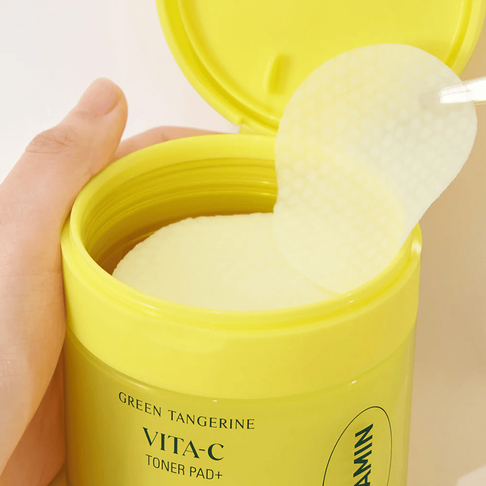 Roka uporablja plastično pinceto za dvig tonirne blazinice s teksturo iz svetlo rumene posode z oznako "GREEN TANGERINE VITA-C TONER PAD+" znamke "goodal".