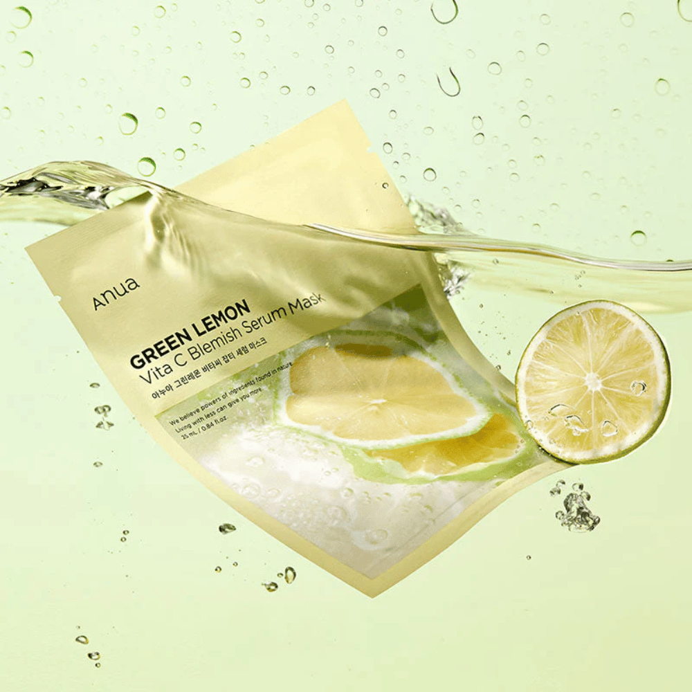 Živahna slika embalaže Anua Green Lemon Vita C Blemish Serum Mask s prozornimi vodnimi kapljicami in rezinami zelene limone naokrog. Embalaža je delno prekrita s tokom vode na svetlo zelenem ozadju.