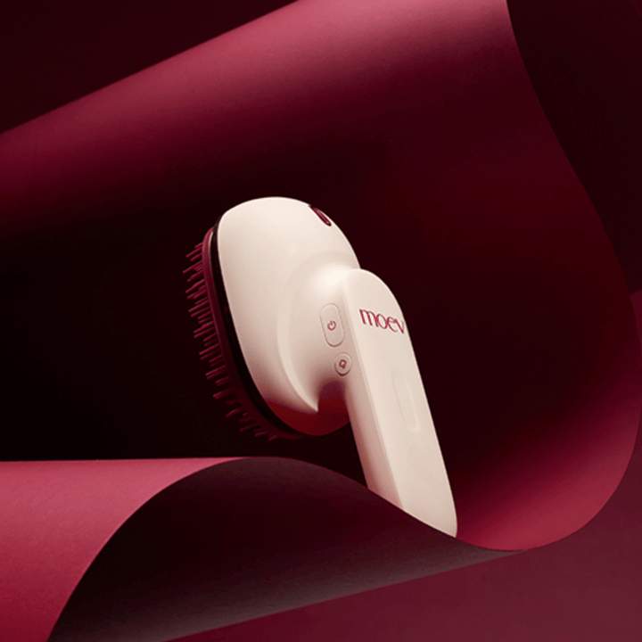 MOEV Hair Steamer Pro v elegantni zasnovi na rdečem ozadju. Inovativna krtača za nego las, ki uporablja paro in toploto za sijaj, mehkobo in okrepljeno zdravje las.