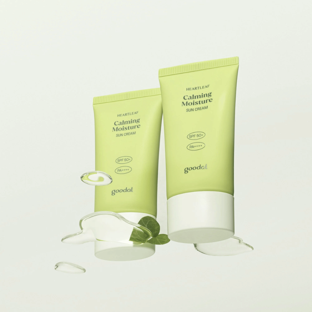 Dve tubi Goodal Heartleaf Calming Moisture Sun Cream SPF50+ PA++++ obdani z rastlinskimi listi in kapljicami seruma na svetlem ozadju.