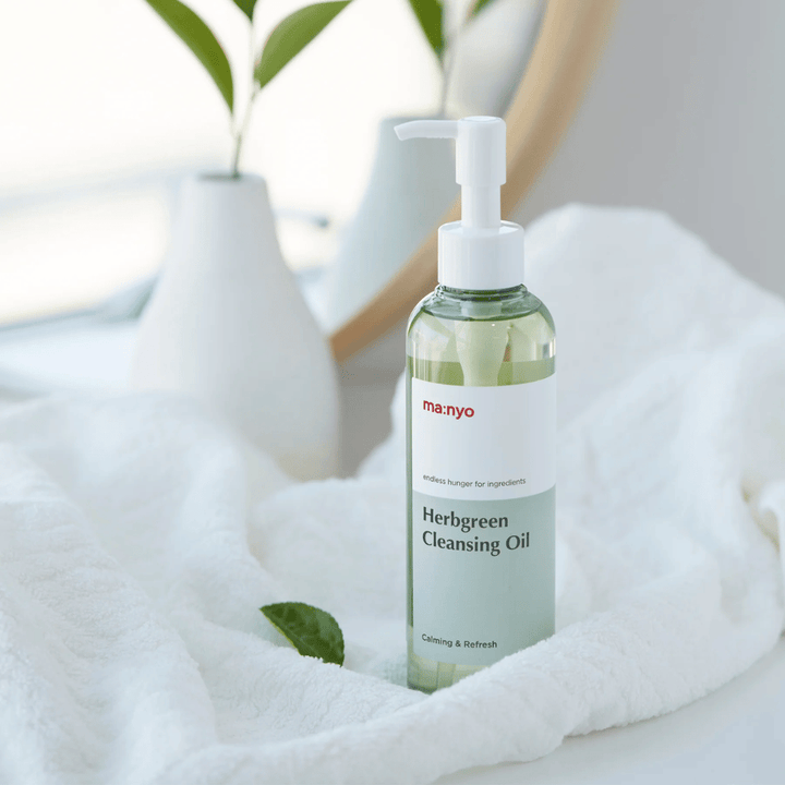 ma:nyo Herbgreen Cleansing Oil v steklenički s črpalko na beli brisači, pomirjujoče čistilno olje z zeliščnimi sestavinami za nežno čiščenje obraza