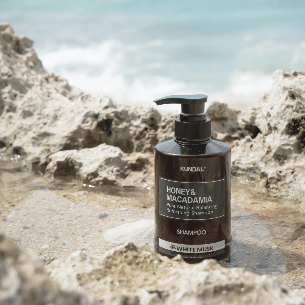 KUNDAL Honey & Macadamia Nature Shampoo White Musk postavljen na skale ob morju, naravni izdelek za nego las s svežim vonjem.