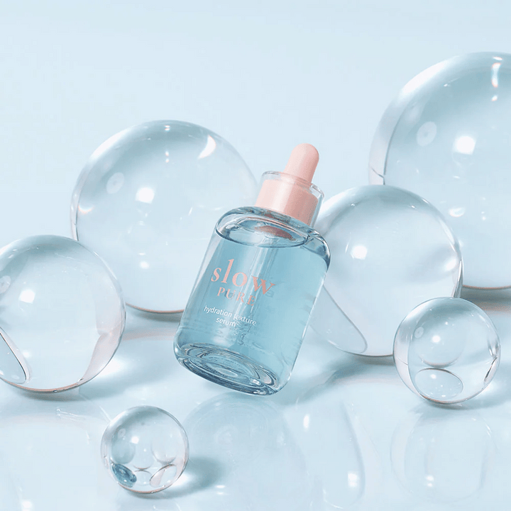 Slow Pure Hydration Texture Serum postavljena med prozorne mehurčke, simbol za intenzivno vlaženje.