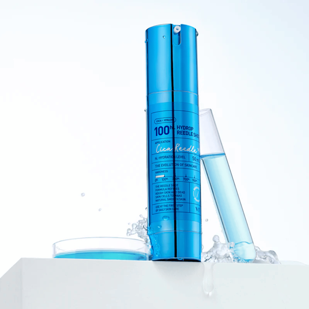 Modra steklenica VT Cica Hyalon Hydrop Reedle Shot 100hL stoji na beli površini z vodnimi kapljicami, poleg epruvete napolnjene z modro tekočino in okroglega pokrovčka z isto tekočino.