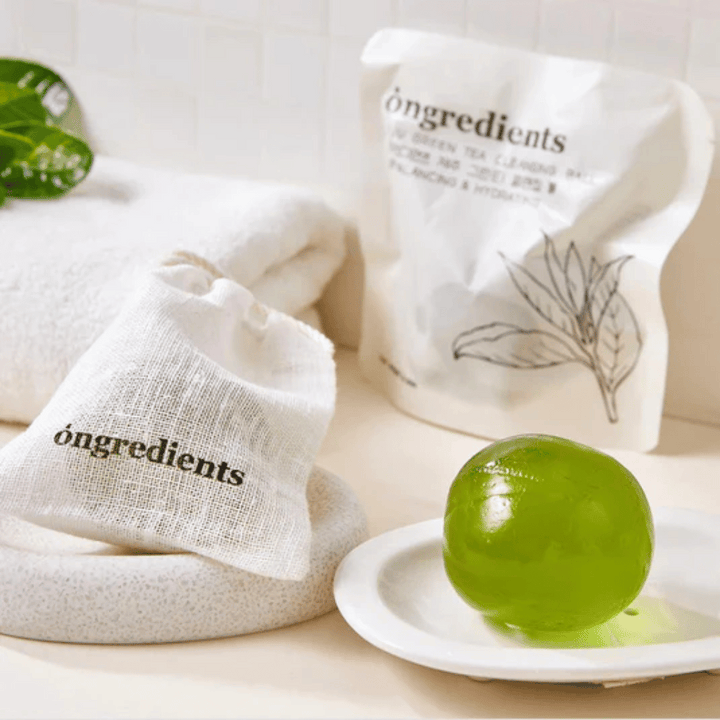 Óngredients Jeju Green Tea Cleansing Ball postavljen na krožnik z embalažo in brisačo – nežno čiščenje z zelenim čajem iz Jejuja.