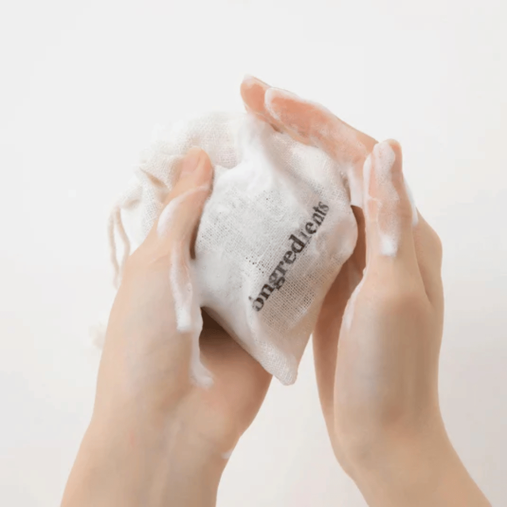 Roke, ki penijo Óngredients Jeju Green Tea Cleansing Ball v tekstilni vrečki – vegansko čiščenje obraza z zelenim čajem.