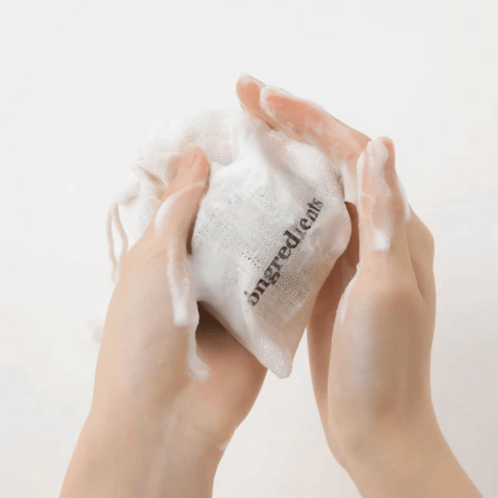 Roke, ki penijo Óngredients Jeju Green Tea Cleansing Ball v tekstilni vrečki – vegansko čiščenje obraza z zelenim čajem.