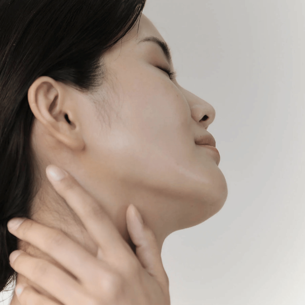 Ženska pokaže svojo pomirjeno, navlaženo kožo po uporabi Celimax Ji Woo Gae Cica BHA Blemish Toner Pad.