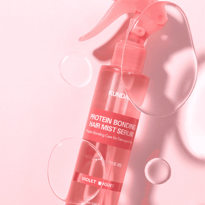 KUNDAL Protein Bonding Hair Mist Serum Violet Bouquet v roza razpršilki, fotografirano na roza ozadju z vodnimi kapljicami.