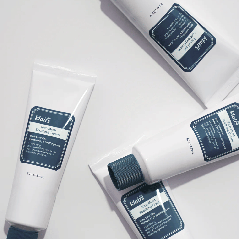 Več tub Klairs Rich Moist Soothing Cream strateško postavljenih na svetli površini, s sencami, ki ustvarjajo globino.