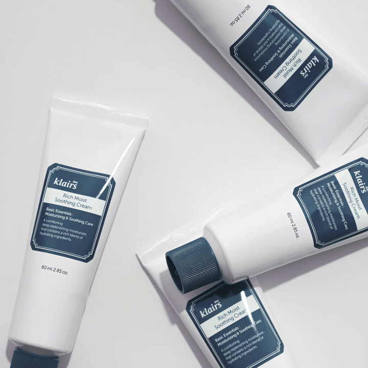 Več tub Klairs Rich Moist Soothing Cream strateško postavljenih na svetli površini, s sencami, ki ustvarjajo globino.