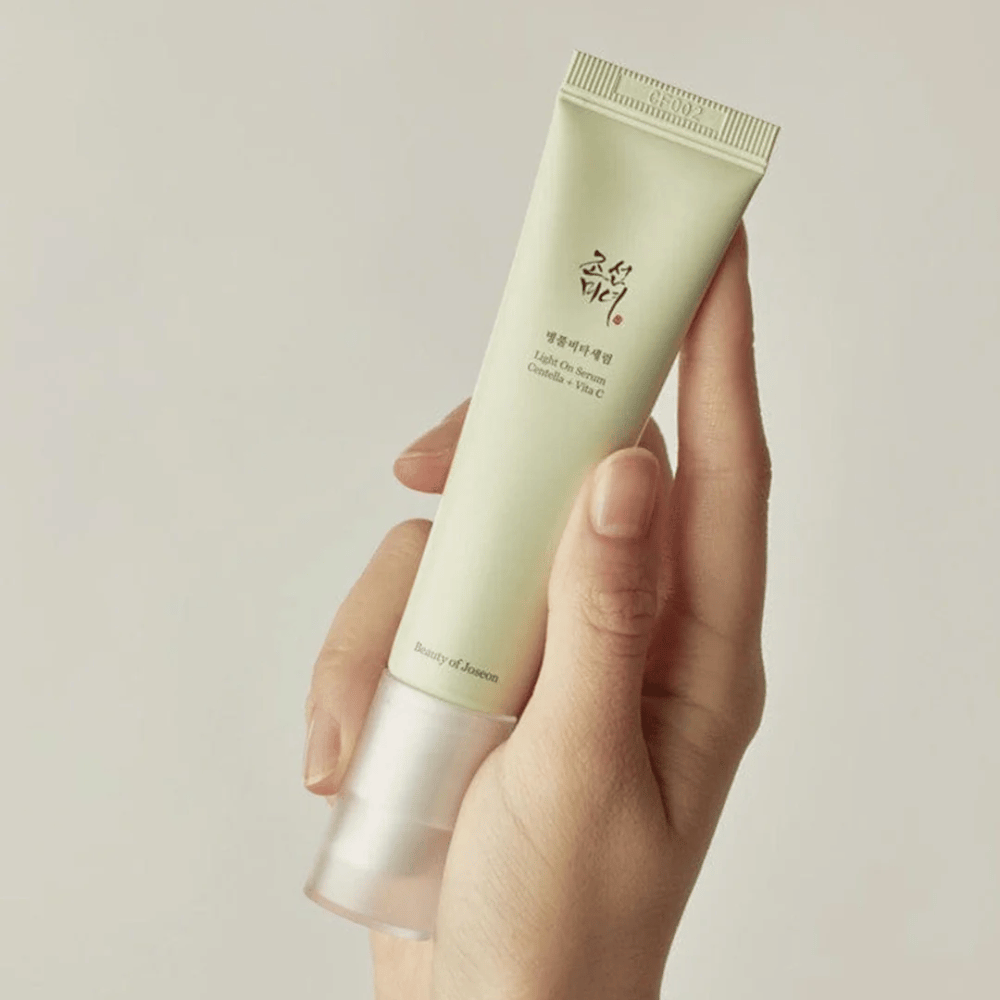 Roka drži Beauty of Joseon Light On Serum s Centello in vitaminom C, v svetlo zeleni tubi z minimalističnim dizajnom na nevtralnem ozadju.