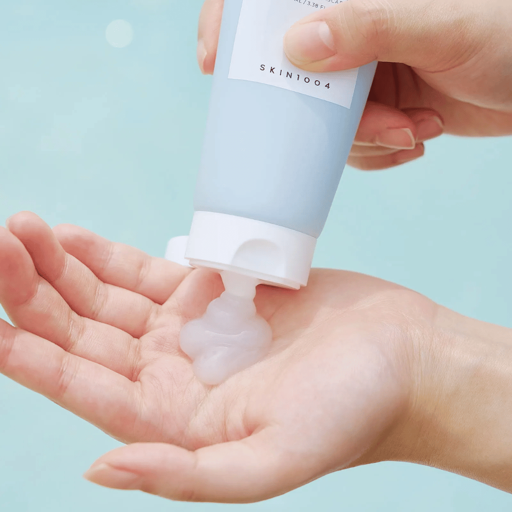 Slika prikazuje nekoga, ki iztiska prozorno gelasto snov iz tube z oznako "SKIN1004 Madagascar Centella Hyalu-Cica Sleeping Pack", ki vsebuje 100 ml izdelka.