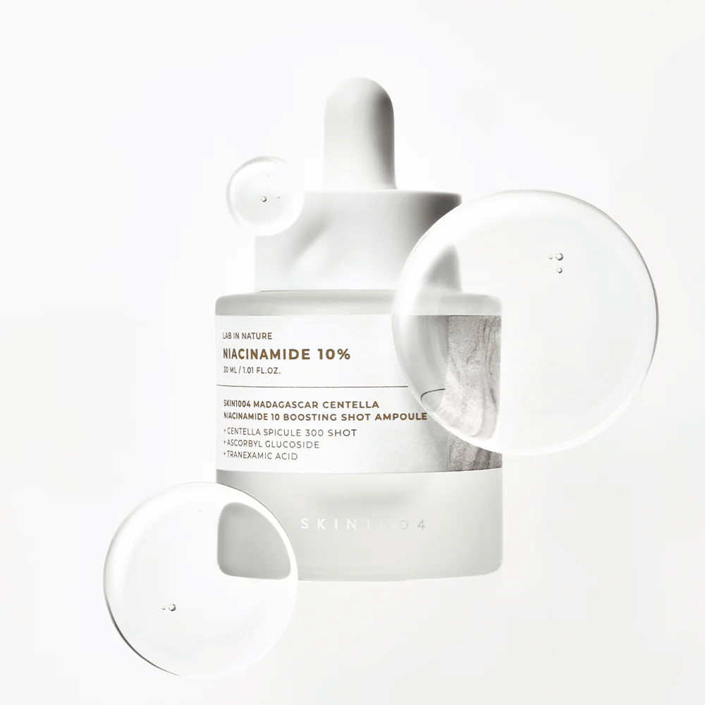 SKIN1004 Madagascar Centella Niacinamide 10 Boosting Shot Ampoule s serumski kapljicami, ki prikazujejo lahko, hitro vpijajočo formulo z niacinamidom, traneksaminsko kislino in centella.