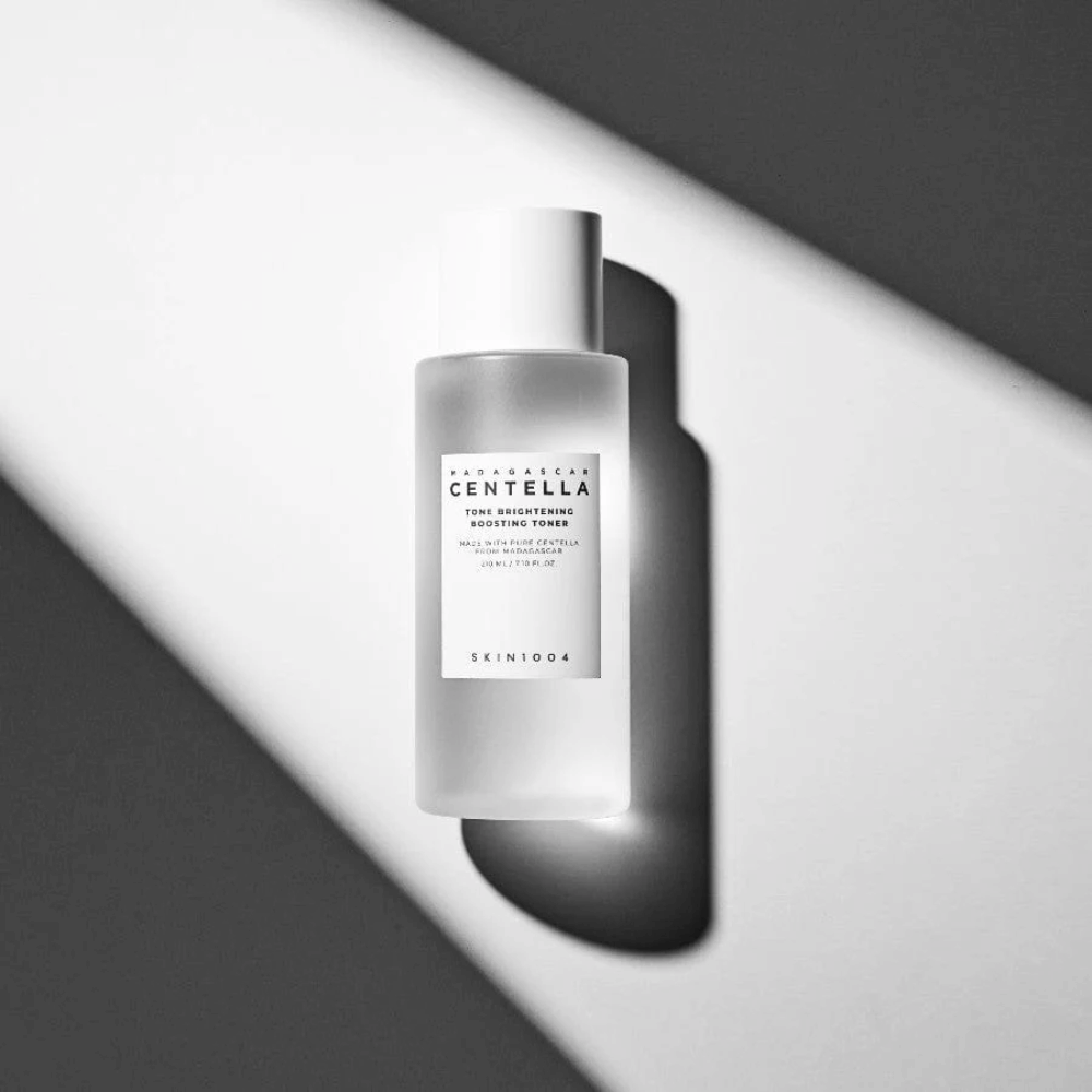 Steklenička SKIN1004 Madagascar Centella Tone Brightening Boosting Toner, ležeča na beli površini z dramatično senco v črno-beli svetlobi.