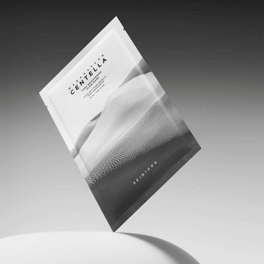 Embalaža Sheet mask znamke SKIN1004 lebdi na sivem ozadju z minimalističnim dizajnom.