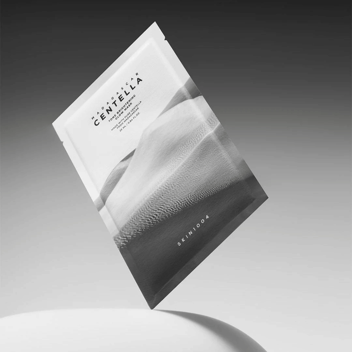 Embalaža Sheet mask znamke SKIN1004 lebdi na sivem ozadju z minimalističnim dizajnom.