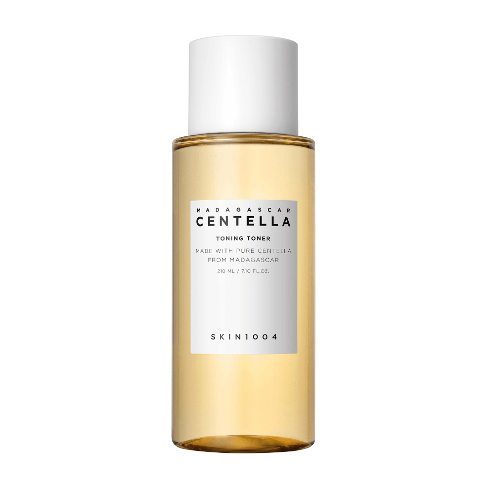 Slika prikazuje steklenico z odtenki za nego kože, označeno "Madagascar Centella Toning Toner" znamke SKIN1004. Izdelek naj bi vseboval 210 ml ali 7.10 fl.oz in je izdelan s čisto centelo iz Madagaskarja. Embalaža je preprosta in elegantna s prozorno steklenico in zlatim toniranim tekočino znotraj, kar daje občutek razkošja in čistosti. Logotip blagovne znamke SKIN1004 je jasno viden v spodnjem delu etikete.