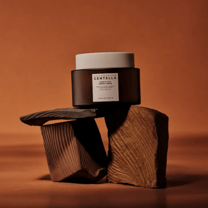 SKIN1004 Madagascar Centella Probio-Cica Enrich Cream v elegantni rjavi stekleni posodi na dekorativnih lesenih blokih – hranljiva korejska obrazna krema, ki krepi kožno pregrado.