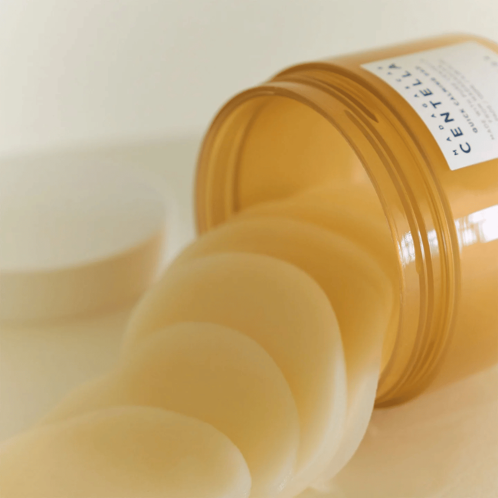 Odprta posoda z SKIN1004 Madagascar Centella Quick Calming Pad – več okroglih tonirnih blazinic v svetlo rumeni tekočini je vidnih, posoda je jantarne barve z belo etiketo.