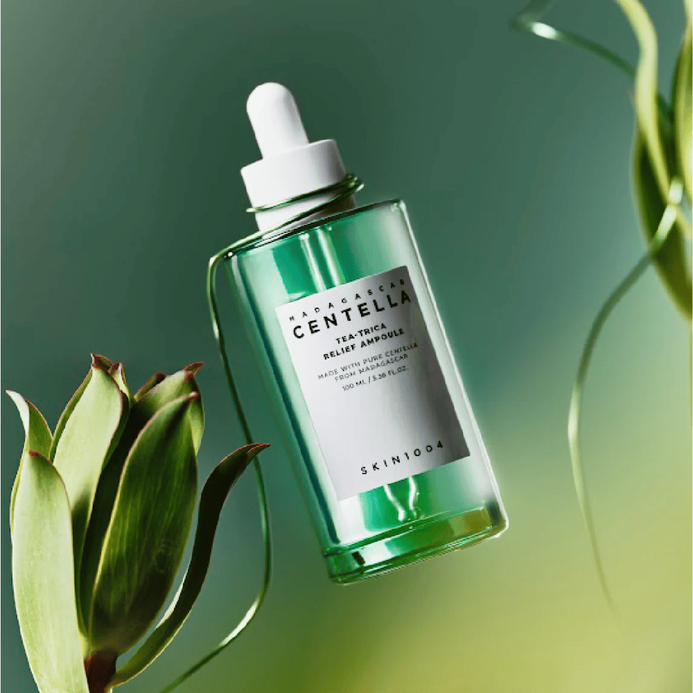SKIN1004 Madagascar Centella Tea-Trica Relief Ampoule – zelena steklenica s pipeto, belo etiketo in 100 ml vsebine, fotografirana proti zelenemu ozadju z rastlinskimi detajli.