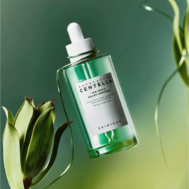 SKIN1004 Madagascar Centella Tea-Trica Relief Ampoule – zelena steklenica s pipeto, belo etiketo in 100 ml vsebine, fotografirana proti zelenemu ozadju z rastlinskimi detajli.