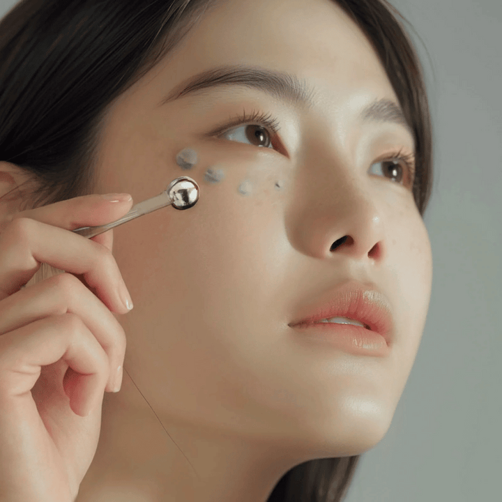 Ženska nanese Heimish Marine Care Algae + Peptide Eye Cream pod oko z metalnim aplikatorjem za hladilni in osvežujoč učinek. Krema pomaga vlažiti in zmanjšati znake staranja okoli oči.