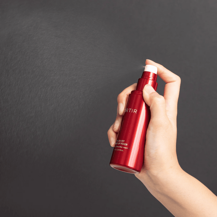 Roka, ki drži rdečo steklenico znamke tirtir Mask Fit Make Up Fixer in razpršuje fin sprej, idealen za fiksiranje ličil.